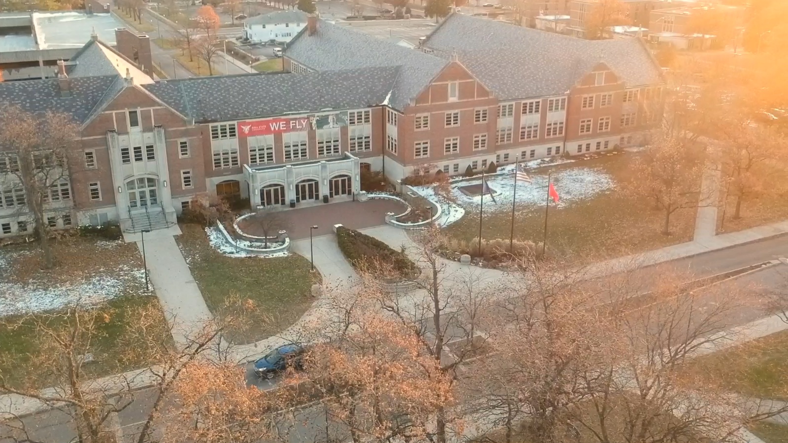Golden-hour drone shot of a campus building with a We Fly banner