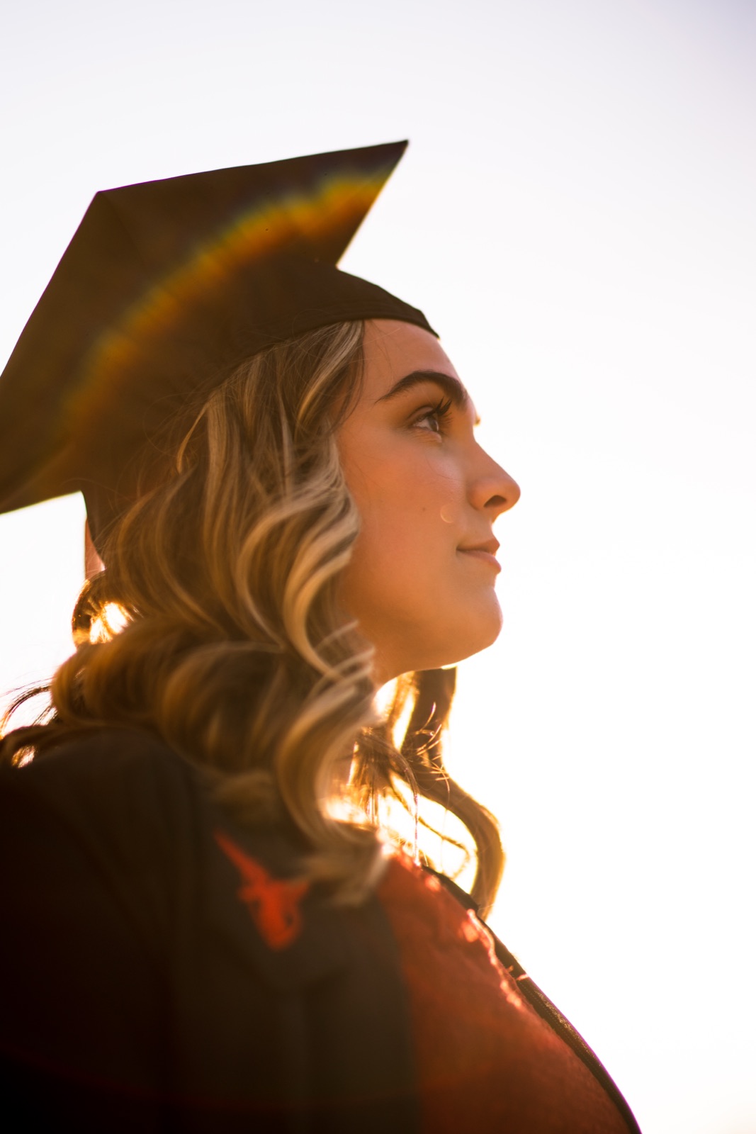 Graduate in cap and gown against a bright sky